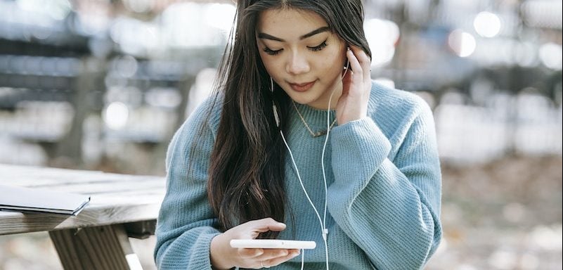 Joven peruana en auriculares con notebook usando smartphone